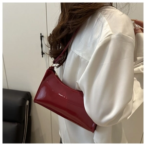 Close-up of a glossy red patent leather baguette bag styled as a retro shoulder bag