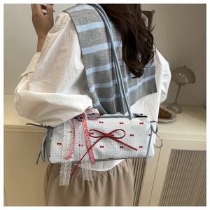 Détail du sac à bandoulière en vichy bleu avec des nœuds rouges et de la dentelle