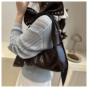 Detail of dark brown glossy leather bag with bow decoration and silver metal studs