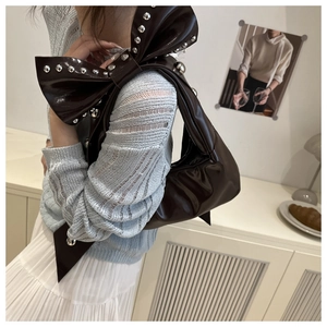 Detail of dark brown glossy shoulder bag with oversized bow and silver rivets