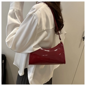 Detail view of a dark red patent leather baguette bag styled as an underarm shoulder bag