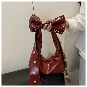 Detail of burgundy glossy leather bag featuring metallic rivets and a bow-shaped handle