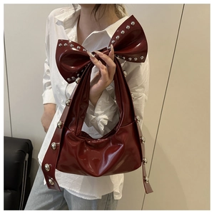 Detail of red bow-shaped tote bag in glossy patent leather with silver rivet decorations
