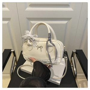 Detail of cream lace Boston bag with metal bow and decorative ribbons on leather chair