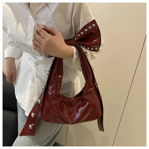 Detail of dark red ribbon bow and silver rivets on a glossy leather shoulder bag