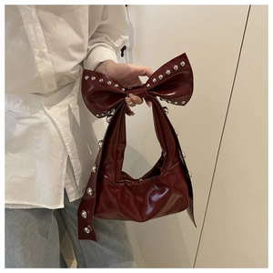 Detail of burgundy faux leather handbag featuring a large bow and silver rivet accents