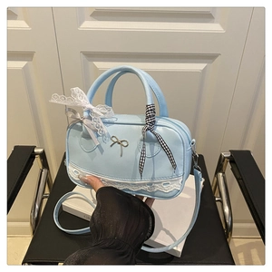 Detail of light blue lace Boston bag with metal bow pendant and decorative ribbons