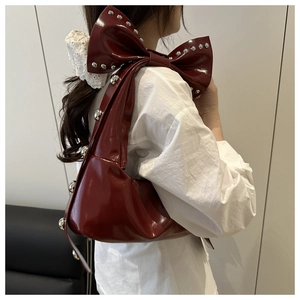 Close-up of wine red patent leather bow shoulder bag with silver rivet details