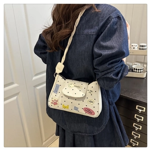 Close-up of a white polka dot crossbody bag with colorful cat patches and woven strap