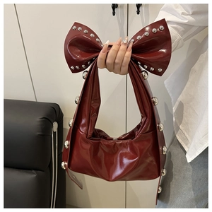 Close-up of deep red glossy handbag with bow handle and silver rivet stud details