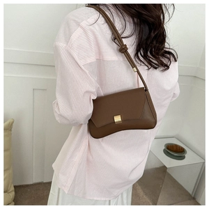 Detail of a brown leather shoulder bag with a gold buckle and knotted strap on a model