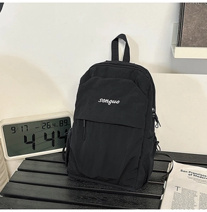 Detail of minimalist black backpack with white songuo logo on a dark wooden table
