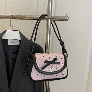 Sac à épaule plissé rose avec nœuds noirs et pendentif cœur sur un cintre