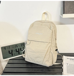 Detail shot of a cream-colored minimalist backpack with songuo text on a black striped desk