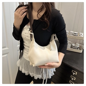 Model wearing a minimalist cream leather hobo shoulder bag with a brown strap detail