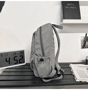 Detailed side view of grey nylon backpack featuring a drawstring side pocket and zipper