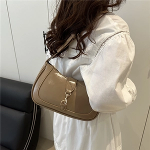 Glossy khaki leather underarm bag with metal clasp shown on model in white lace shirt