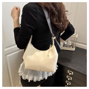 Cream shoulder bag with brown leather strap worn by a model in an indoor setting