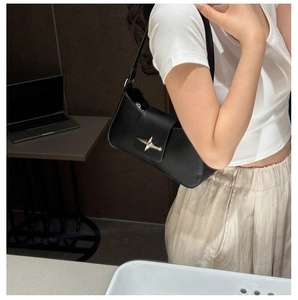 Detail of black leather underarm bag featuring a silver star-shaped metal clasp buckle
