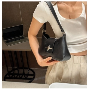 Detail of a black leather underarm bag featuring a silver star-shaped metal buckle on the flap