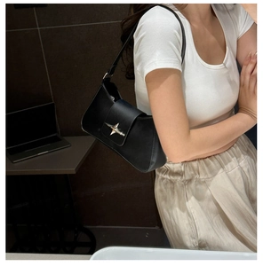 Detail of a black faux leather shoulder bag with a metallic silver star buckle on the flap