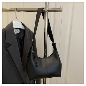 Detail of a black hobo shoulder bag with silver zipper and strap on a gray blazer