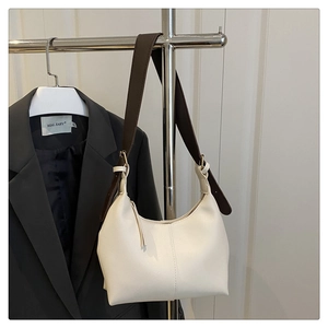 Detailed shot of white half-moon shoulder bag with adjustable brown strap and tassel