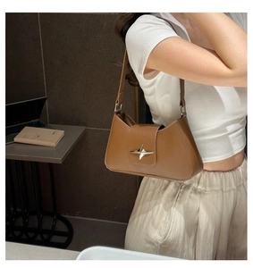 Detail of caramel brown underarm bag showing glossy leather and silver star buckle