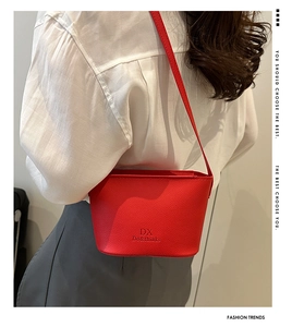 Detail of red bucket bag in lychee pattern leather with a thin shoulder strap on a model