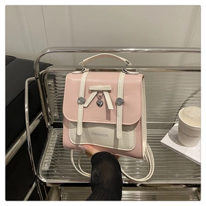 Detail of pink and beige mini backpack with white bow and heart charm on metal chair