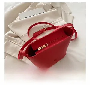Detail of red bucket bag with gold zipper and brand logo on a cream blazer background