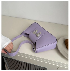 Detail of purple shoulder bag featuring a large silver metal bow and leather strap