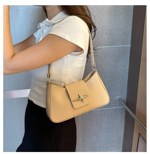Detail of minimalist beige underarm bag featuring a metallic gold star emblem buckle