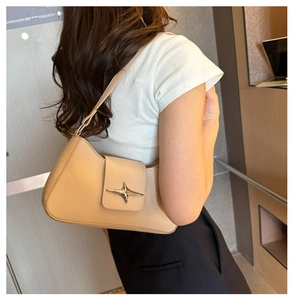 Model wearing a chic beige leather shoulder bag with a metallic star buckle detail