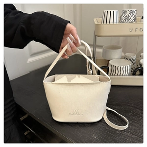Close-up of white bucket bag featuring premium lychee texture and brand logo detail