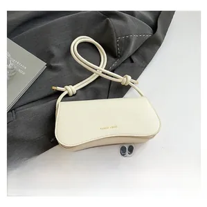 Detail of a creamy white pebbled leather bag with knotted strap and gold logo lettering