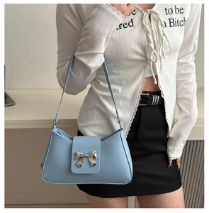 Detail of light blue faux leather underarm bag featuring a metallic silver bow accent