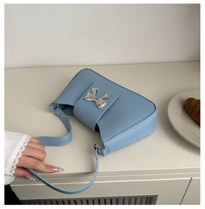 Detail of light blue crescent shoulder bag featuring a silver metal bow accent