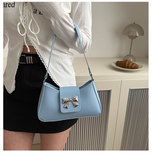 Detail of light blue handbag with silver bow hardware worn as a shoulder bag