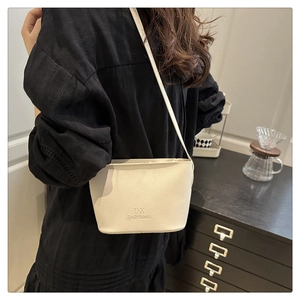 Detail of a creamy white crossbody bucket bag with textured lychee grain and leather strap