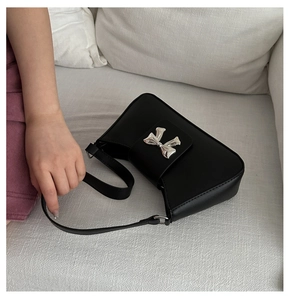 Detail shot of the silver bow buckle and smooth black leather texture on a chic baguette bag