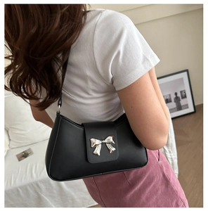 Side view of black faux leather underarm bag with decorative silver bow buckle on model