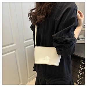 White lychee leather shoulder bag with logo detail worn over a black dress on a model