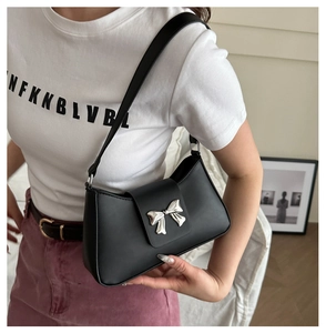 Close-up of a black leather underarm bag featuring a silver 3D bow buckle and slim strap