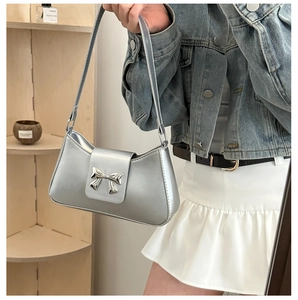 Detail of silver metallic underarm bag featuring a 3D metal bow clasp and sleek leather finish