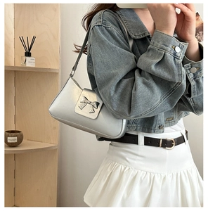 Detailed view of silver metallic shoulder bag featuring a prominent metal bow buckle