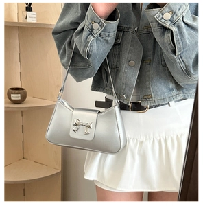 Silver metallic saddle bag featuring a stylish metal bow detail worn over the shoulder
