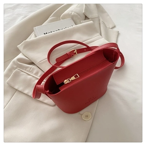 Top-down view of a red textured leather bucket bag on a white suit with adjustable strap