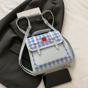Dettaglio del tessuto a quadri blu con ricamo a mela rossa sullo zaino alla moda