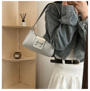 Detail of silver metallic shoulder bag featuring a 3D metal bow and wide strap design